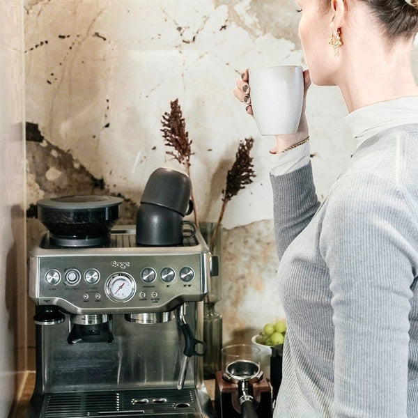 En kvinna dricker kaffe vid sin espressomaskin